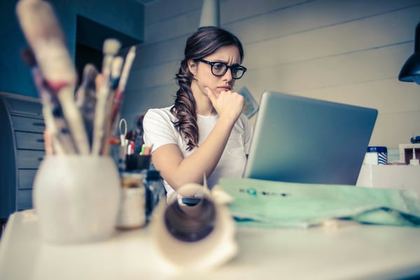A businesswoman sitting at her desk looks thoughtfully at her laptop