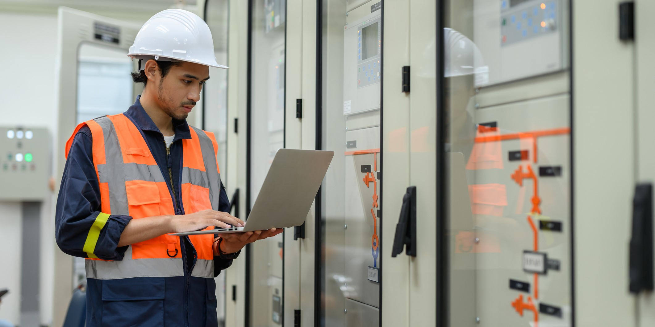 Male electrical technician uses a laptop computer to check the status of a control panel switch board in the control room of an electric transformer station